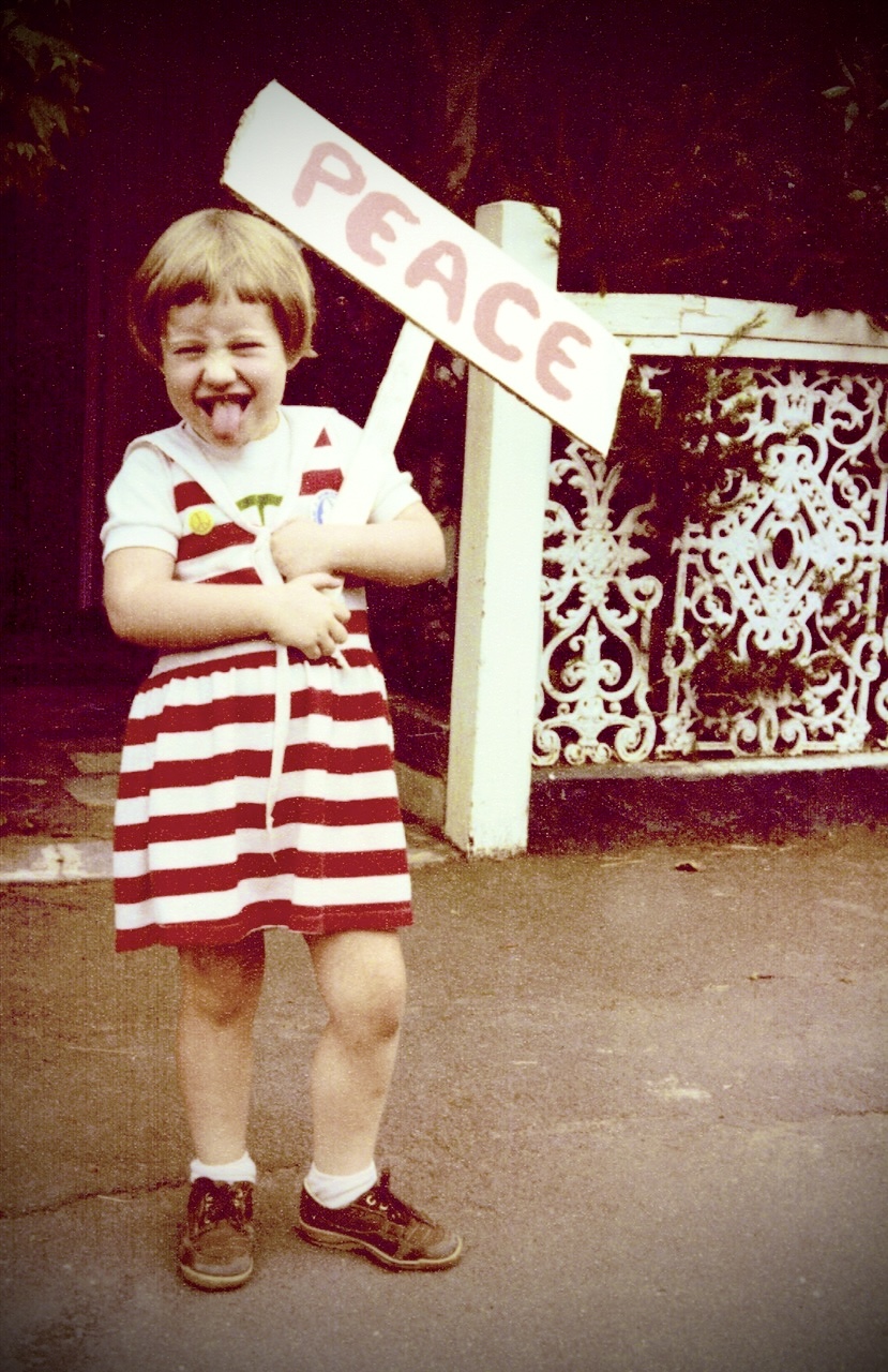 Catherine as a 7 year old holding a sign that reads 'peace'